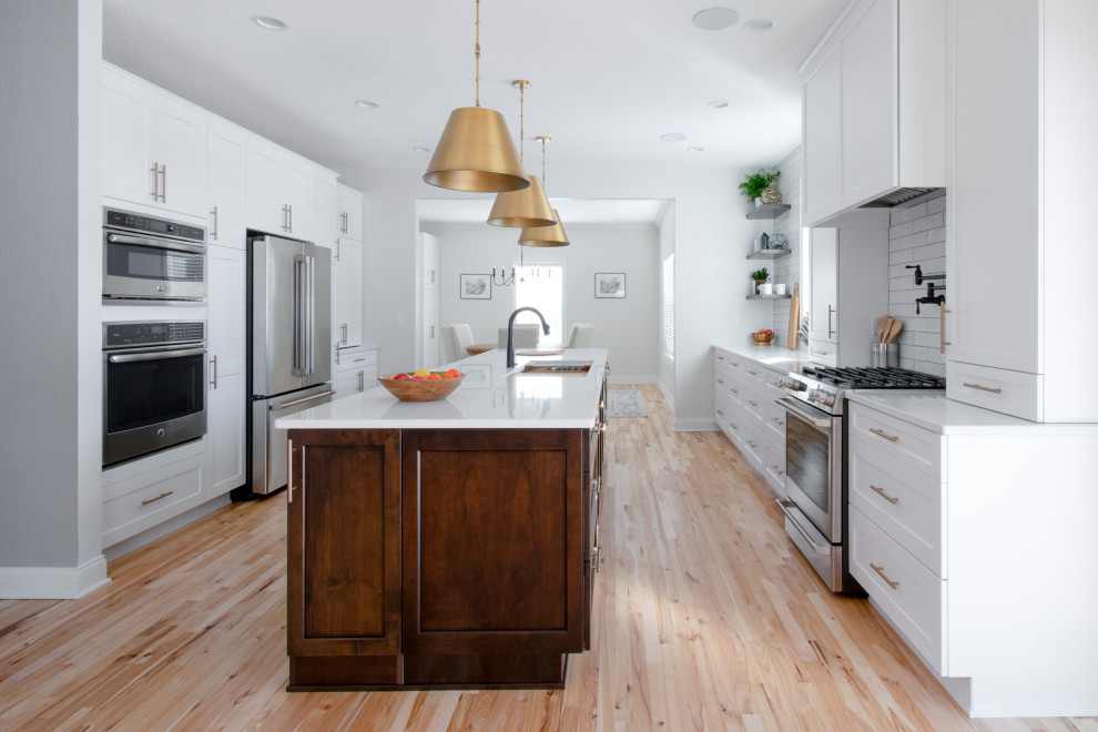 Large trendy galley light wood floor and brown floor eat-in kitchen photo in Milwaukee with an undermount sink, shaker cabinets, white cabinets, quartz countertops, white backsplash, subway tile backsplash, stainless steel appliances, an island and white countertops