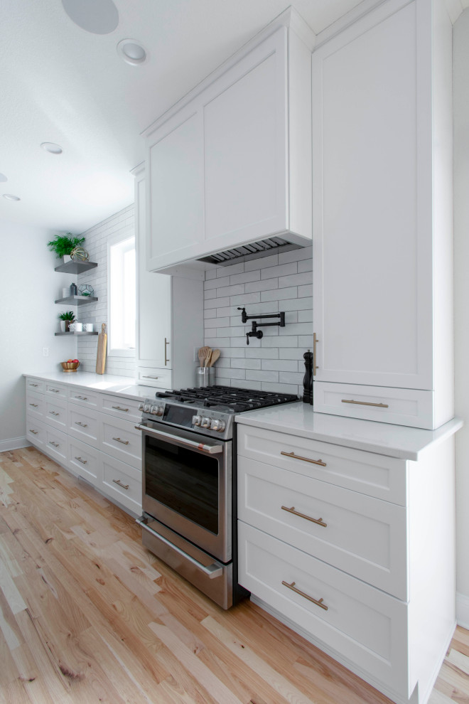 Inspiration for a large contemporary galley light wood floor and brown floor eat-in kitchen remodel in Milwaukee with an undermount sink, shaker cabinets, white cabinets, quartz countertops, white backsplash, subway tile backsplash, stainless steel appliances, an island and white countertops