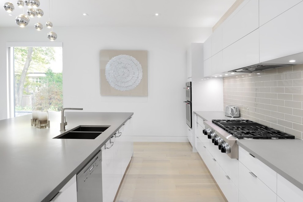 Modern inredning av ett mellanstort kök, med en dubbel diskho, släta luckor, vita skåp, grått stänkskydd, stänkskydd i tunnelbanekakel, rostfria vitvaror, en köksö och beiget golv