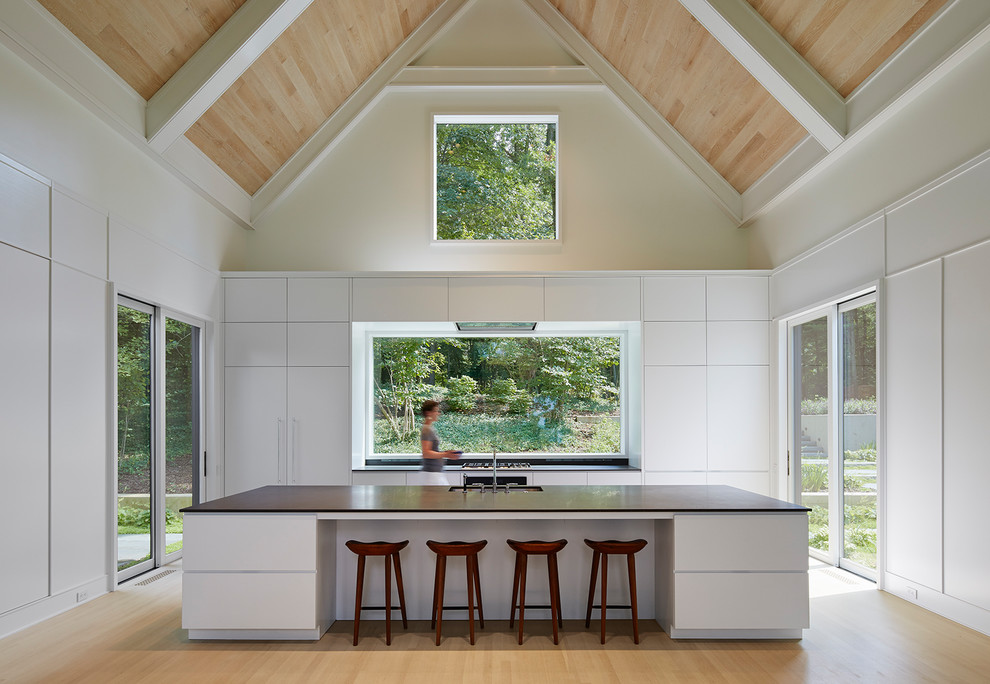 Idéer för ett modernt kök, med en undermonterad diskho, släta luckor, vita skåp, fönster som stänkskydd, ljust trägolv, en köksö och beiget golv