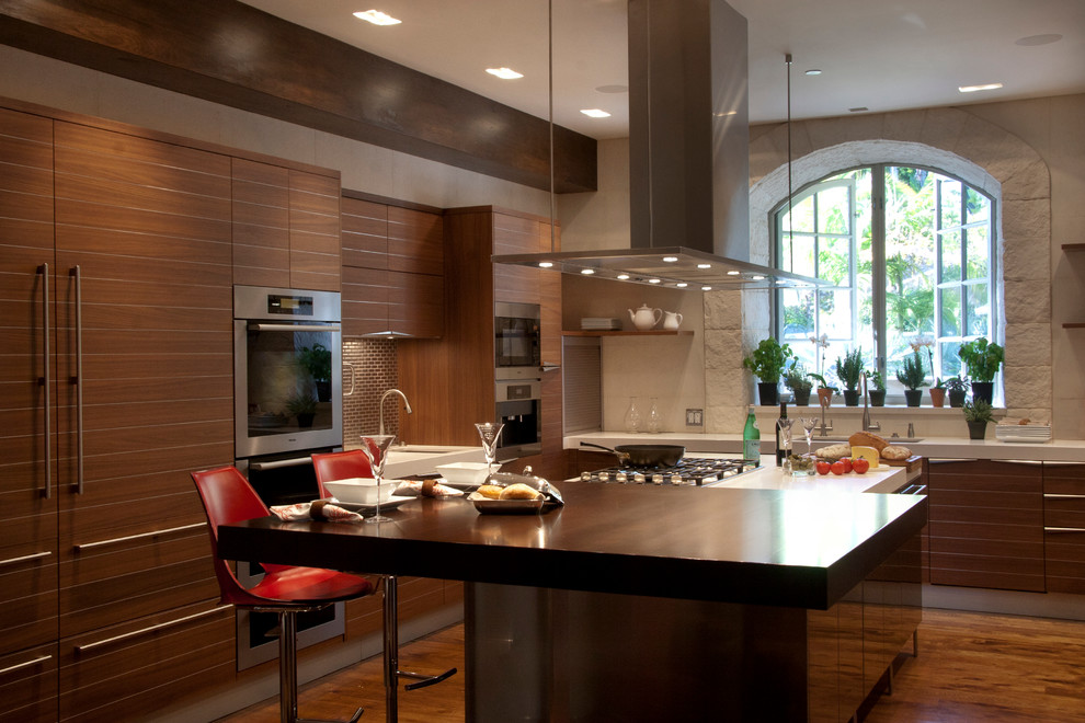 Inspiration for a large contemporary u-shaped kitchen/diner in Los Angeles with flat-panel cabinets, medium wood cabinets, engineered stone countertops, beige splashback, glass tiled splashback, stainless steel appliances, medium hardwood flooring and an island.