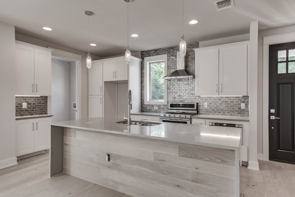 Inspiration for a mid-sized contemporary l-shaped light wood floor and beige floor open concept kitchen remodel in Austin with shaker cabinets, white cabinets, an island, a double-bowl sink, solid surface countertops, gray backsplash, subway tile backsplash, stainless steel appliances and gray countertops