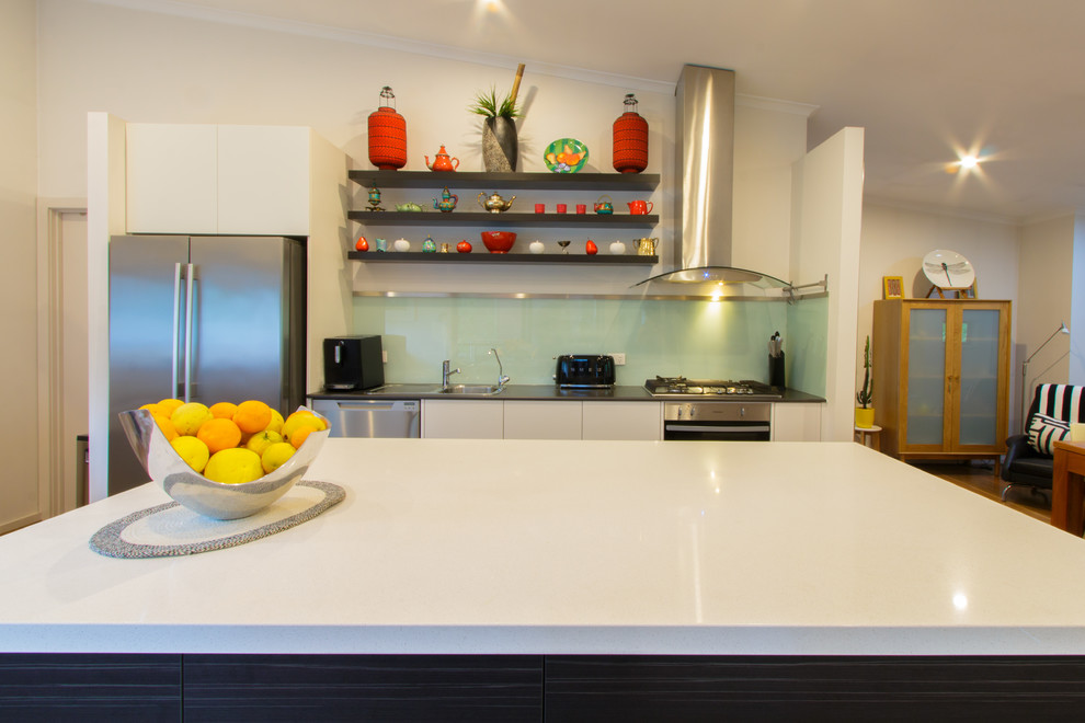 Mittelgroße Moderne Küche mit Quarzwerkstein-Arbeitsplatte, Einbauwaschbecken, weißen Schränken, Küchenrückwand in Grün, Glasrückwand, Küchengeräten aus Edelstahl, braunem Holzboden, Kücheninsel, braunem Boden und weißer Arbeitsplatte in Adelaide