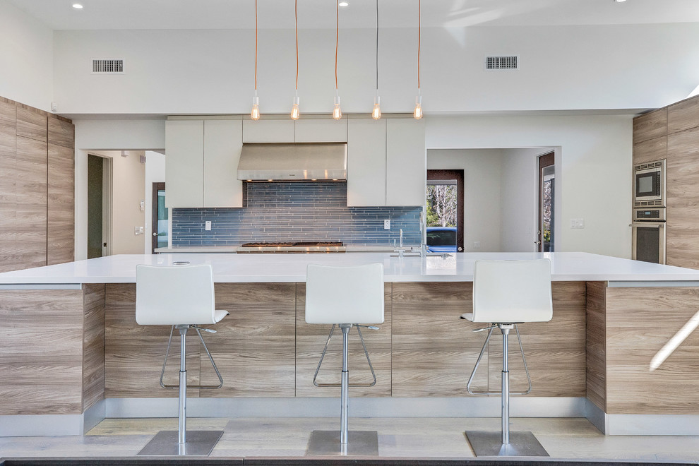 Photo of a large contemporary u-shaped kitchen/diner in Los Angeles with a submerged sink, flat-panel cabinets, light wood cabinets, quartz worktops, blue splashback, glass tiled splashback, stainless steel appliances, an island and white worktops.