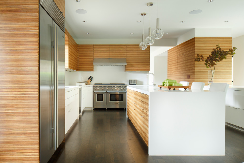 Cette image montre une cuisine design en bois brun de taille moyenne avec un placard à porte plane, un plan de travail en surface solide, un électroménager en acier inoxydable, parquet foncé et îlot.