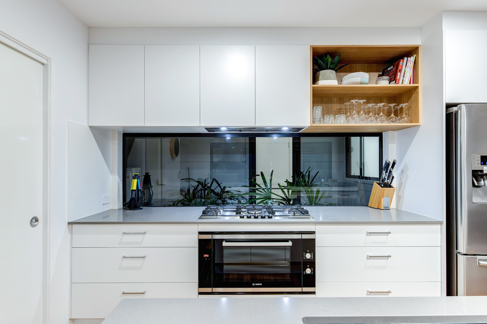 Idéer för att renovera ett mellanstort funkis vit vitt kök och matrum, med en dubbel diskho, vita skåp, bänkskiva i kvarts, fönster som stänkskydd, svarta vitvaror, ljust trägolv, en köksö, brunt golv och luckor med upphöjd panel