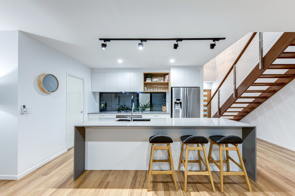 Modern inredning av ett mellanstort grå grått kök, med en undermonterad diskho, släta luckor, vita skåp, fönster som stänkskydd, rostfria vitvaror, ljust trägolv, en köksö, beiget golv och bänkskiva i kvarts