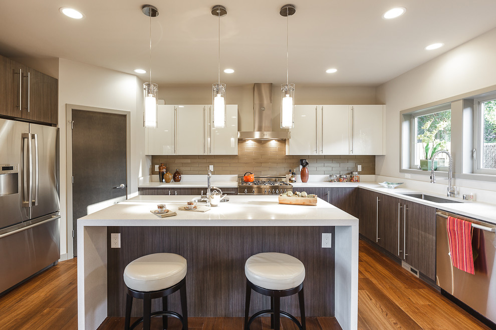 This is an example of a large contemporary grey and cream u-shaped kitchen/diner in Seattle with a submerged sink, flat-panel cabinets, grey cabinets, engineered stone countertops, white splashback, metro tiled splashback, stainless steel appliances, medium hardwood flooring and an island.