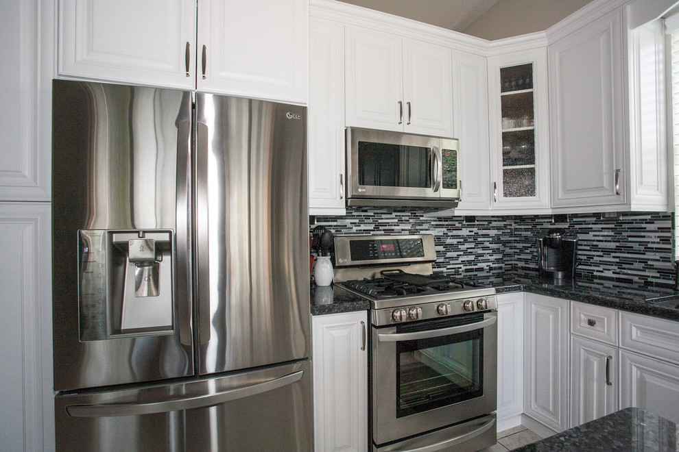 Example of a trendy l-shaped eat-in kitchen design in Miami with an undermount sink, recessed-panel cabinets, white cabinets, granite countertops, multicolored backsplash and stainless steel appliances