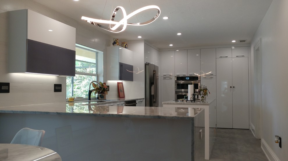 Design ideas for a contemporary kitchen in Tampa with a submerged sink, flat-panel cabinets, white cabinets, marble worktops, white splashback, ceramic splashback, stainless steel appliances, porcelain flooring, an island and grey floors.