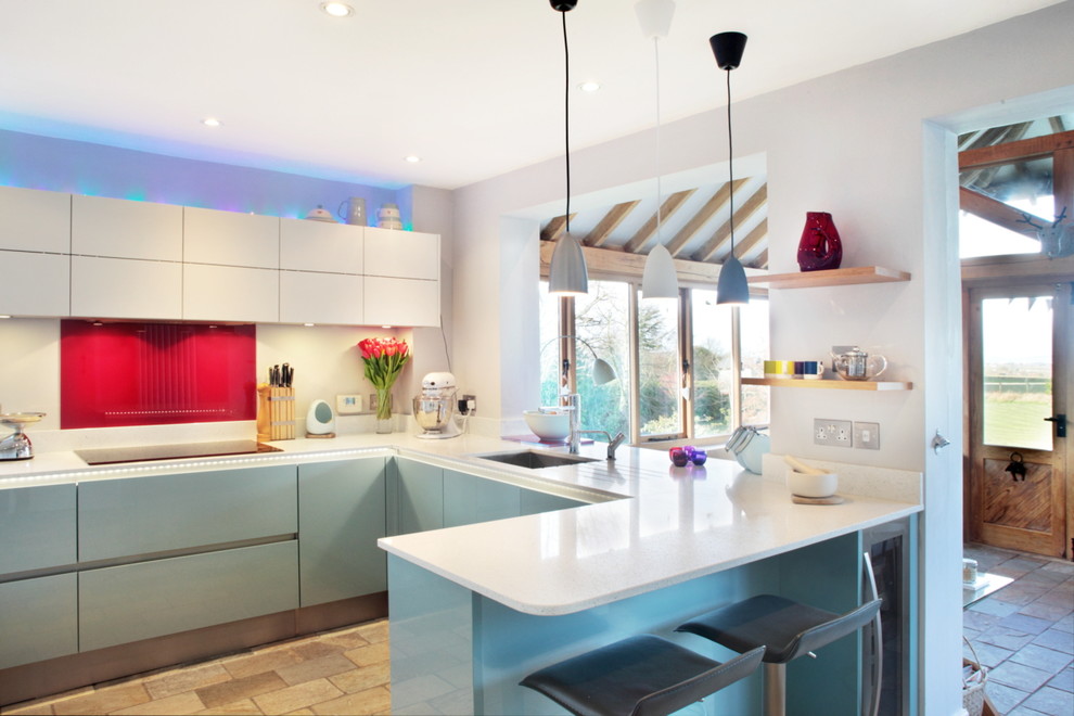 Idee per una cucina minimal di medie dimensioni con ante lisce, ante blu, paraspruzzi rosso, paraspruzzi con piastrelle di vetro e elettrodomestici in acciaio inossidabile