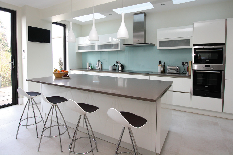 Moderne Küche mit weißen Schränken, Quarzwerkstein-Arbeitsplatte, Küchenrückwand in Blau, Küchengeräten aus Edelstahl und Kücheninsel in London