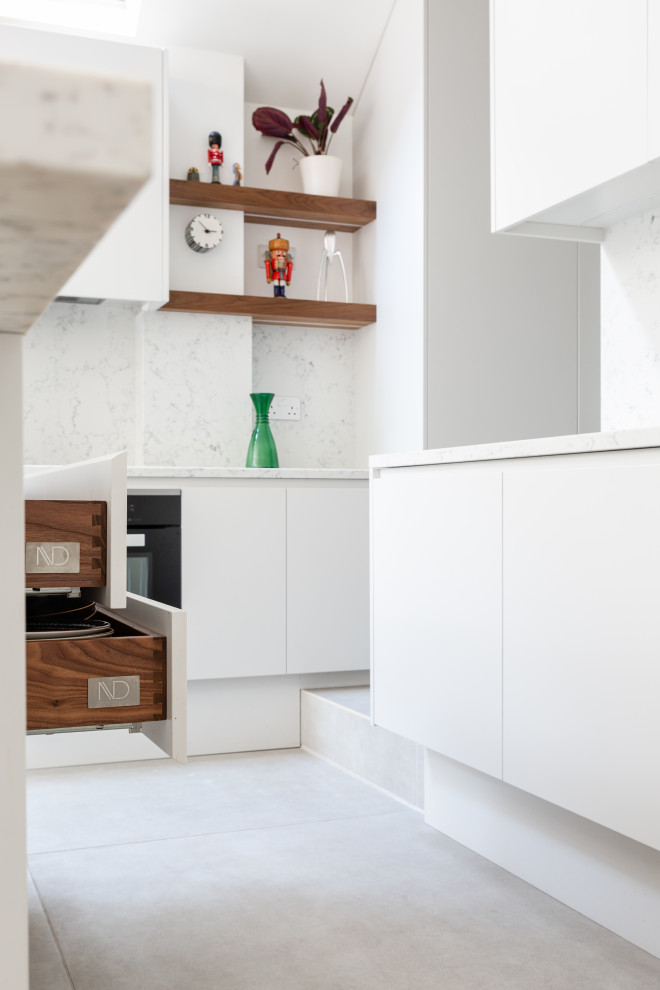 Modern inredning av ett mellanstort vit vitt kök och matrum, med en nedsänkt diskho, släta luckor, vita skåp, marmorbänkskiva, vitt stänkskydd, stänkskydd i marmor, svarta vitvaror, klinkergolv i keramik, en köksö och vitt golv