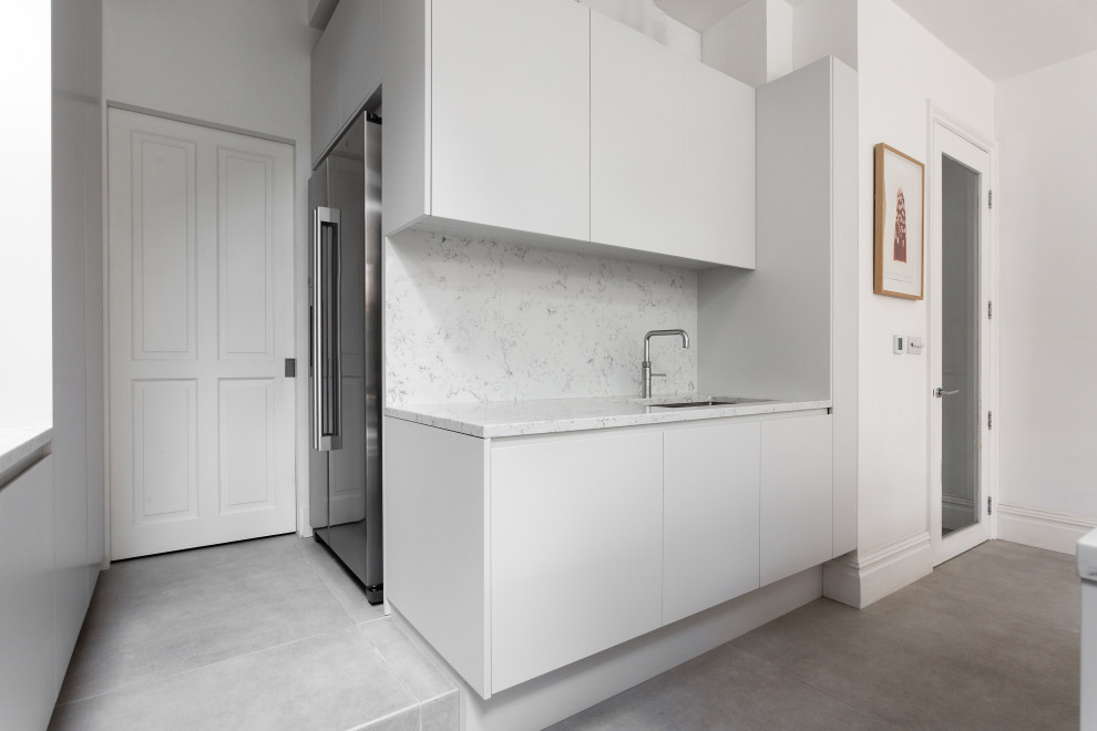 Medium sized contemporary kitchen/diner in London with a built-in sink, flat-panel cabinets, white cabinets, marble worktops, white splashback, marble splashback, black appliances, ceramic flooring, an island, white floors and white worktops.