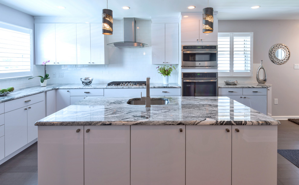 Inredning av ett klassiskt mellanstort grå grått kök, med en undermonterad diskho, släta luckor, vita skåp, granitbänkskiva, vitt stänkskydd, stänkskydd i tunnelbanekakel, rostfria vitvaror, mellanmörkt trägolv, en köksö och brunt golv
