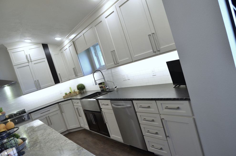 Moderne Wohnküche mit Landhausspüle, Schrankfronten im Shaker-Stil, weißen Schränken, Küchenrückwand in Weiß, Rückwand aus Metrofliesen, Küchengeräten aus Edelstahl, Kücheninsel und braunem Boden in Sonstige