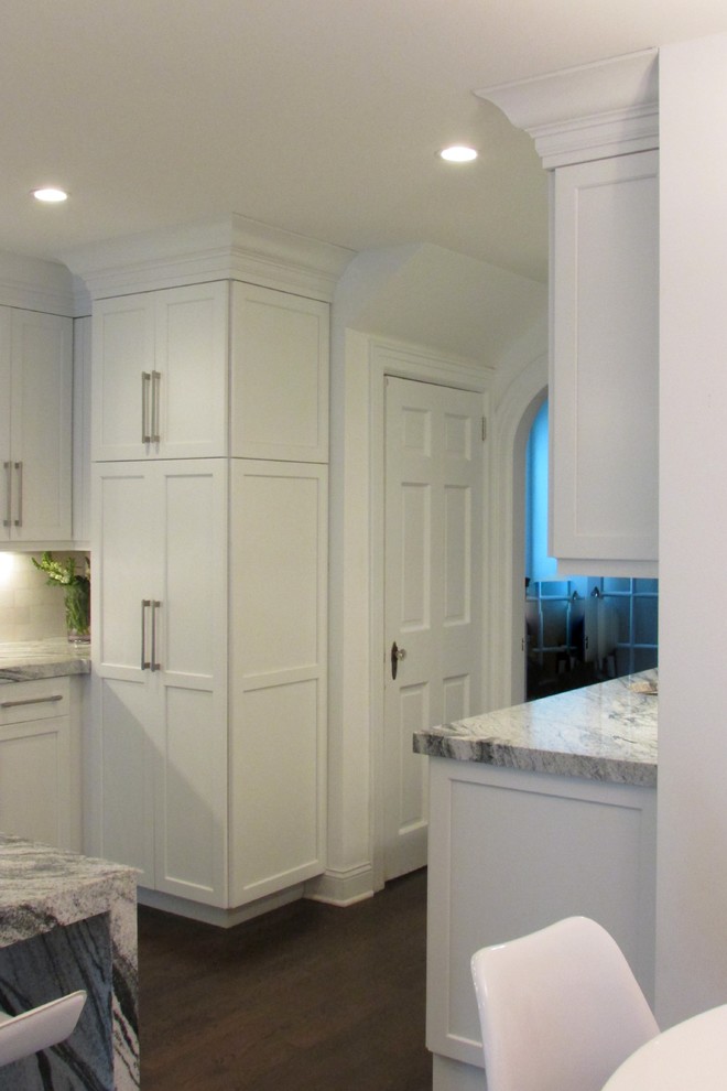 Large transitional l-shaped dark wood floor enclosed kitchen photo in New York with white cabinets, white backsplash, stainless steel appliances, an island, a double-bowl sink, shaker cabinets, marble countertops and subway tile backsplash