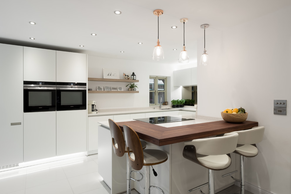 Immagine di una piccola cucina design con lavello sottopiano, ante lisce, ante bianche, penisola, pavimento bianco e elettrodomestici neri