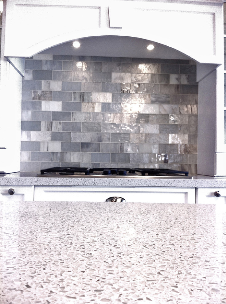 Idéer för att renovera ett mellanstort funkis vit vitt kök, med luckor med infälld panel, vita skåp, bänkskiva i återvunnet glas, stänkskydd med metallisk yta, stänkskydd i glaskakel och en köksö