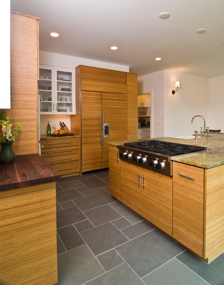 Modelo de cocina comedor actual con fregadero sobremueble, armarios con paneles lisos, puertas de armario de madera oscura, encimera de granito, electrodomésticos de acero inoxidable, suelo de pizarra y una isla