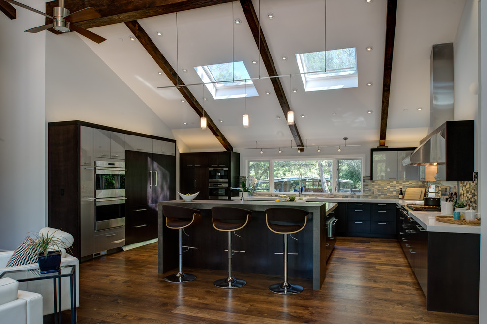 Photo of an expansive contemporary l-shaped kitchen/diner in San Francisco with a submerged sink, flat-panel cabinets, brown cabinets, engineered stone countertops, multi-coloured splashback, mosaic tiled splashback, stainless steel appliances, dark hardwood flooring and an island.