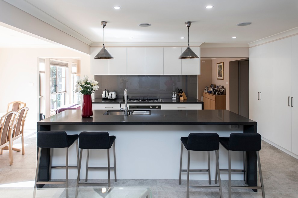 Idéer för att renovera ett stort funkis grå grått kök med öppen planlösning, med en undermonterad diskho, släta luckor, vita skåp, bänkskiva i kvarts, stänkskydd med metallisk yta, glaspanel som stänkskydd, rostfria vitvaror, klinkergolv i porslin, en köksö och grått golv