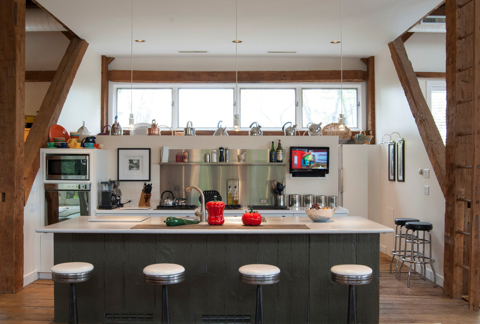 Cette photo montre une cuisine nature en inox avec un placard sans porte, une crédence métallisée, un électroménager en acier inoxydable, un sol en bois brun et îlot.