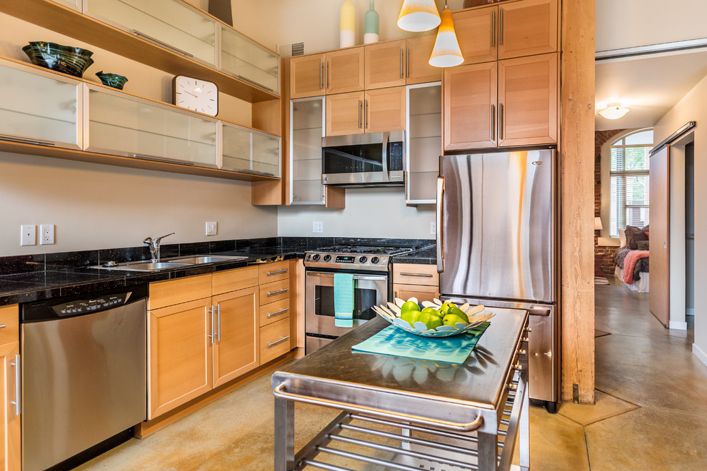 Moderne Küche in L-Form mit Doppelwaschbecken, Schrankfronten im Shaker-Stil, hellen Holzschränken, Küchenrückwand in Schwarz, Küchengeräten aus Edelstahl, Betonboden und Kücheninsel in Denver
