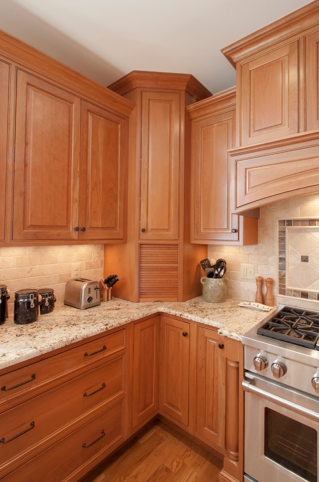 Inredning av ett klassiskt kök, med luckor med profilerade fronter, skåp i ljust trä, granitbänkskiva, beige stänkskydd och rostfria vitvaror