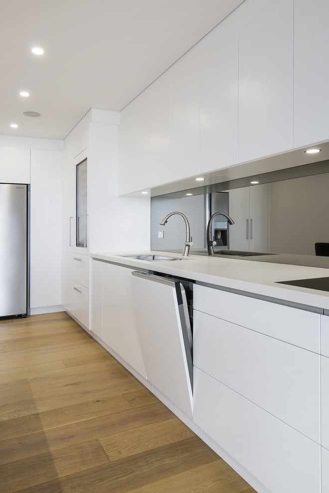 Exempel på ett stort skandinaviskt kök, med en undermonterad diskho, släta luckor, vita skåp, bänkskiva i kvarts, stänkskydd med metallisk yta, spegel som stänkskydd, svarta vitvaror, ljust trägolv, en köksö och gult golv