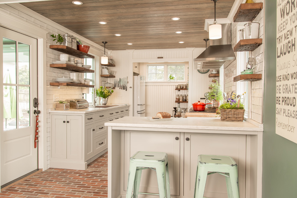 Cottage brick floor and red floor kitchen photo in Bridgeport with an undermount sink, shaker cabinets, white cabinets, white backsplash, subway tile backsplash, stainless steel appliances, white countertops and a peninsula
