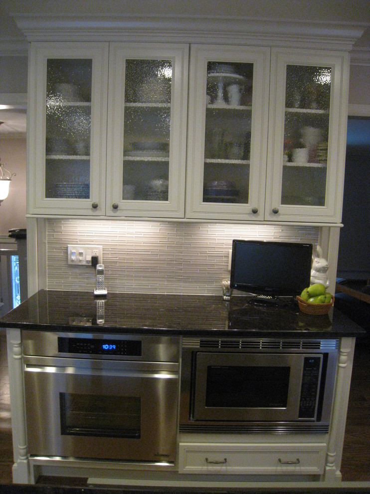 Example of a mid-sized transitional l-shaped medium tone wood floor enclosed kitchen design in New York with an undermount sink, recessed-panel cabinets, white cabinets, quartz countertops, gray backsplash, ceramic backsplash, stainless steel appliances and an island