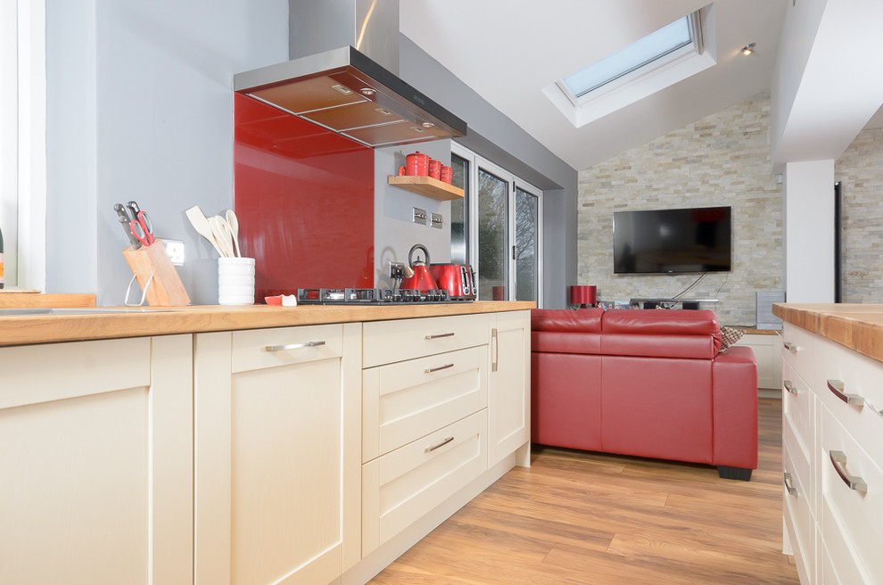 Photo of a large l-shaped open plan kitchen in Other with light wood cabinets, wood worktops, red splashback, glass sheet splashback, integrated appliances, light hardwood flooring and an island.