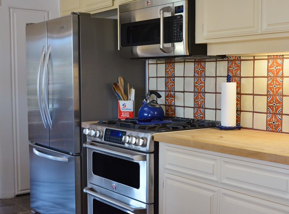 Mittelgroße Mediterrane Küche mit profilierten Schrankfronten, Arbeitsplatte aus Holz, Küchenrückwand in Gelb, Rückwand aus Keramikfliesen, Küchengeräten aus Edelstahl und Terrakottaboden in San Diego