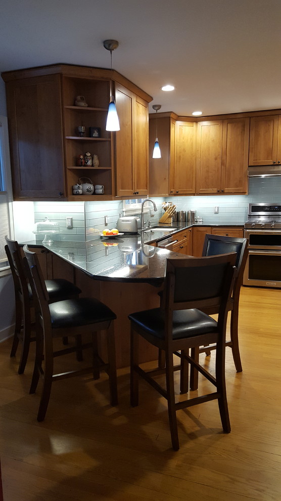 Example of a mid-sized transitional u-shaped medium tone wood floor eat-in kitchen design in Other with an undermount sink, shaker cabinets, light wood cabinets, granite countertops, blue backsplash, glass tile backsplash, stainless steel appliances and no island