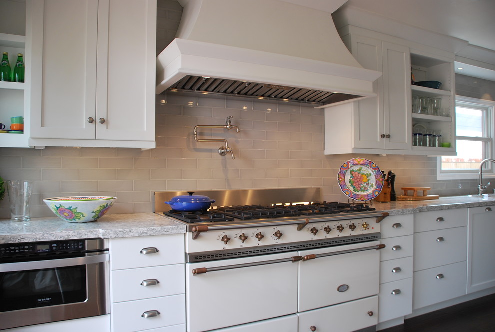 Photo of a medium sized traditional galley enclosed kitchen in Orange County with a belfast sink, shaker cabinets, white cabinets, engineered stone countertops, grey splashback, ceramic splashback, white appliances, dark hardwood flooring, brown floors and multicoloured worktops.