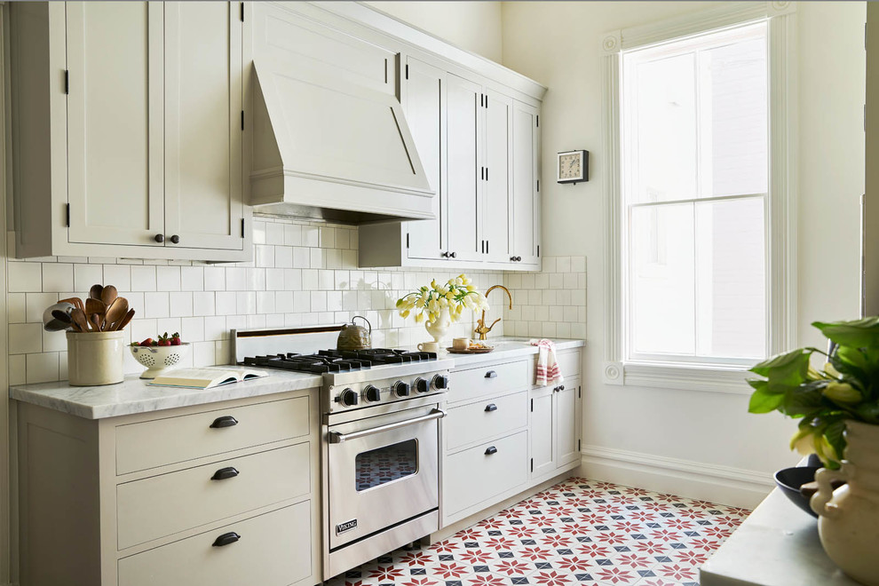 サンフランシスコにあるトラディショナルスタイルのおしゃれなII型キッチン (アンダーカウンターシンク、シェーカースタイル扉のキャビネット、ベージュのキャビネット、白いキッチンパネル、シルバーの調理設備、赤い床) の写真