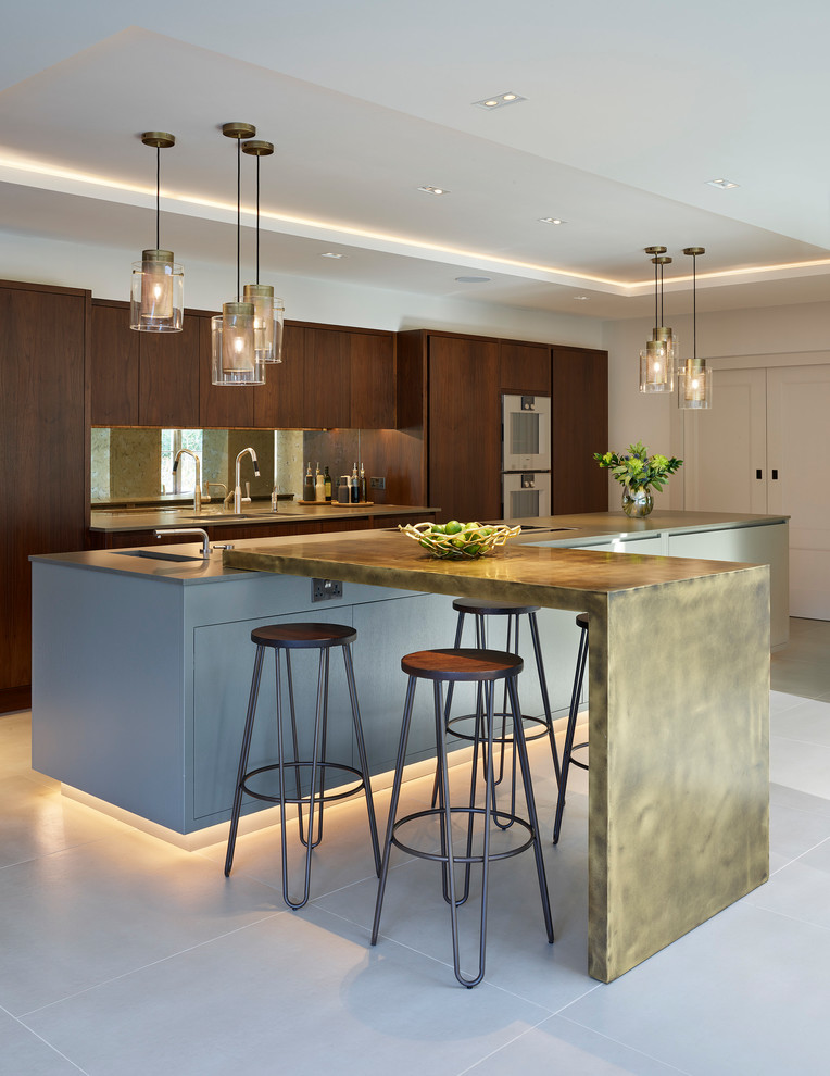 This is an example of an expansive contemporary l-shaped open plan kitchen in Kent with flat-panel cabinets, dark wood cabinets, a double-bowl sink, quartz worktops, metallic splashback, mirror splashback, stainless steel appliances, ceramic flooring, an island and beige floors.