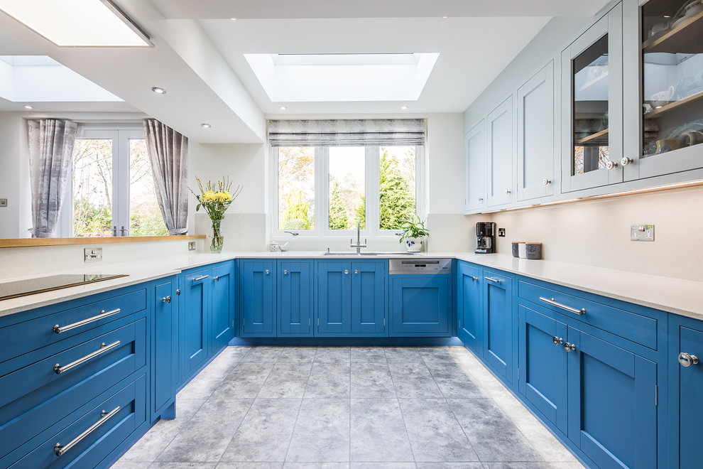 This is an example of a large traditional u-shaped kitchen/diner in Other with a double-bowl sink, shaker cabinets, blue cabinets, white splashback, glass sheet splashback, integrated appliances, lino flooring, a breakfast bar, grey floors and white worktops.
