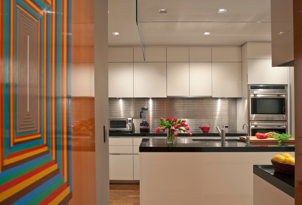 Mid-sized trendy u-shaped medium tone wood floor enclosed kitchen photo in New York with flat-panel cabinets, metallic backsplash, metal backsplash, an undermount sink, granite countertops, stainless steel appliances, an island and black countertops