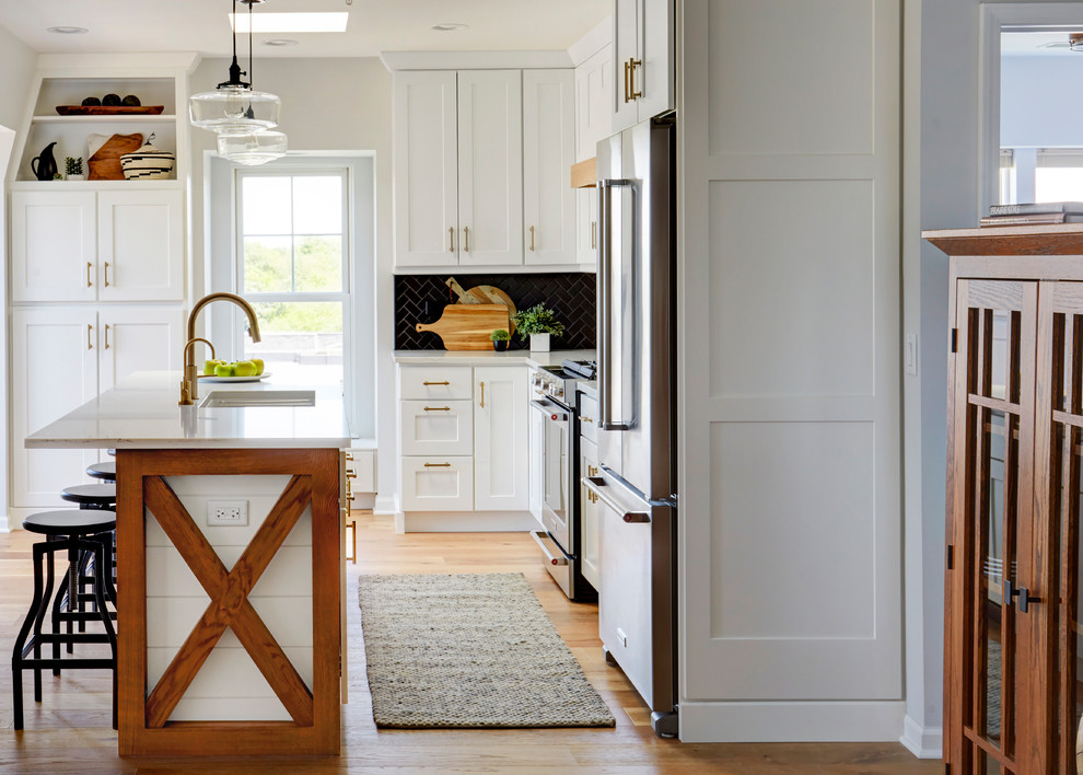 Bild på ett mellanstort maritimt vit vitt kök, med en undermonterad diskho, skåp i shakerstil, vita skåp, bänkskiva i kvarts, svart stänkskydd, stänkskydd i keramik, rostfria vitvaror, mellanmörkt trägolv, en köksö och brunt golv