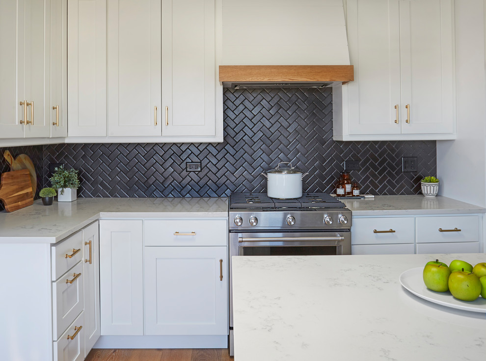 Photo of a medium sized nautical l-shaped kitchen in Chicago with a submerged sink, shaker cabinets, white cabinets, engineered stone countertops, black splashback, ceramic splashback, stainless steel appliances, medium hardwood flooring, an island, brown floors and white worktops.