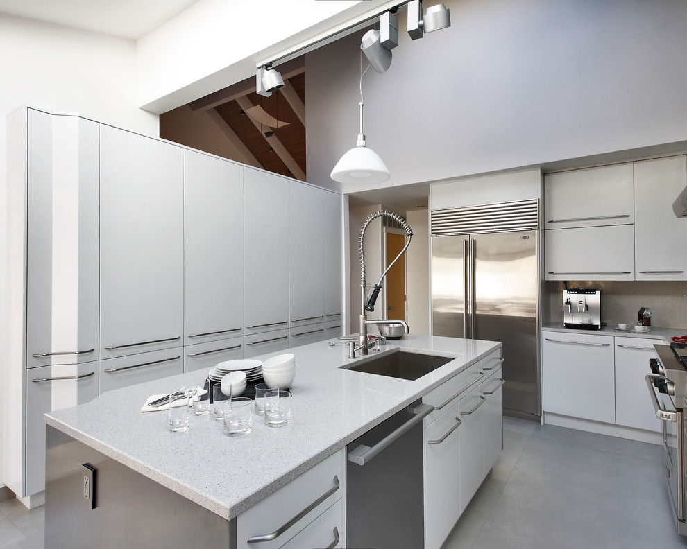 Bild på ett mellanstort funkis l-kök, med en undermonterad diskho, rostfria vitvaror, betonggolv, släta luckor, vita skåp, granitbänkskiva, grått stänkskydd och en köksö