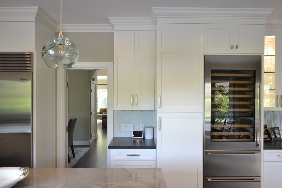 Bild på ett stort vintage vit vitt kök, med en enkel diskho, luckor med infälld panel, vita skåp, granitbänkskiva, vitt stänkskydd, stänkskydd i porslinskakel, rostfria vitvaror, mellanmörkt trägolv, en köksö och brunt golv