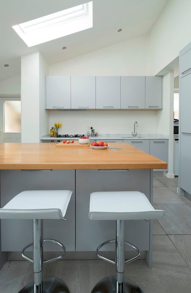 Inspiration for a medium sized contemporary single-wall kitchen/diner in Cardiff with a built-in sink, flat-panel cabinets, grey cabinets, composite countertops, glass sheet splashback, stainless steel appliances, ceramic flooring and an island.