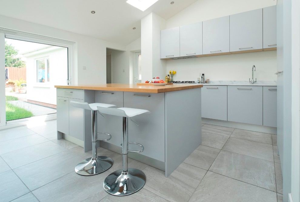 Photo of a medium sized contemporary single-wall kitchen/diner in Cardiff with a built-in sink, flat-panel cabinets, grey cabinets, composite countertops, glass sheet splashback, stainless steel appliances, ceramic flooring and an island.