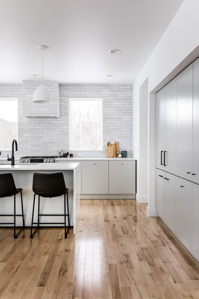 Inspiration for a large contemporary l-shaped light wood floor and brown floor kitchen remodel in Grand Rapids with an undermount sink, flat-panel cabinets, gray cabinets, quartzite countertops, gray backsplash, brick backsplash, stainless steel appliances, an island and white countertops
