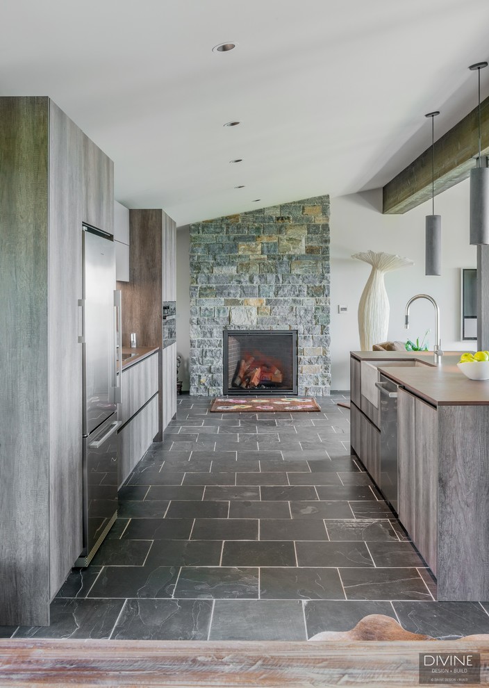 Idéer för att renovera ett stort eklektiskt brun linjärt brunt kök med öppen planlösning, med en rustik diskho, släta luckor, skåp i mörkt trä, granitbänkskiva, stänkskydd med metallisk yta, glaspanel som stänkskydd, rostfria vitvaror, skiffergolv, en köksö och grått golv