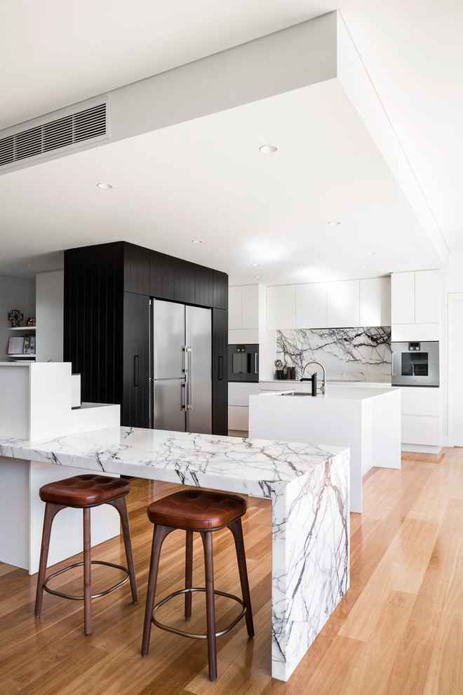Foto på ett funkis kök, med en undermonterad diskho, släta luckor, vitt stänkskydd, rostfria vitvaror, mellanmörkt trägolv, en köksö och brunt golv