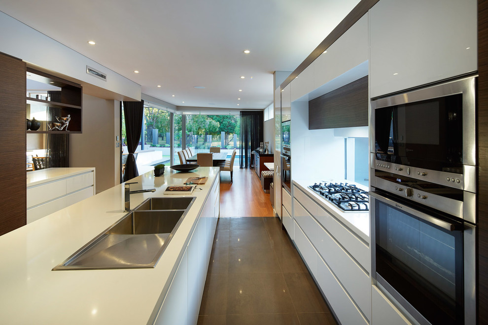 This is an example of a large contemporary l-shaped open plan kitchen in Other with a built-in sink, flat-panel cabinets, white cabinets, engineered stone countertops, glass sheet splashback, stainless steel appliances, ceramic flooring and an island.